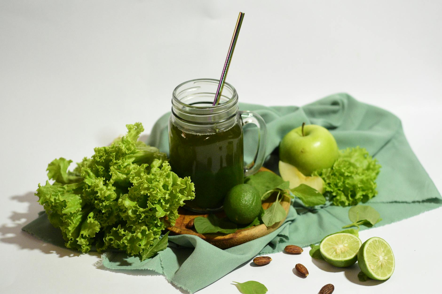 A vibrant green juice surrounded by fresh apples, limes, and lettuce, served in a mason jar with a metal straw. - how to detox