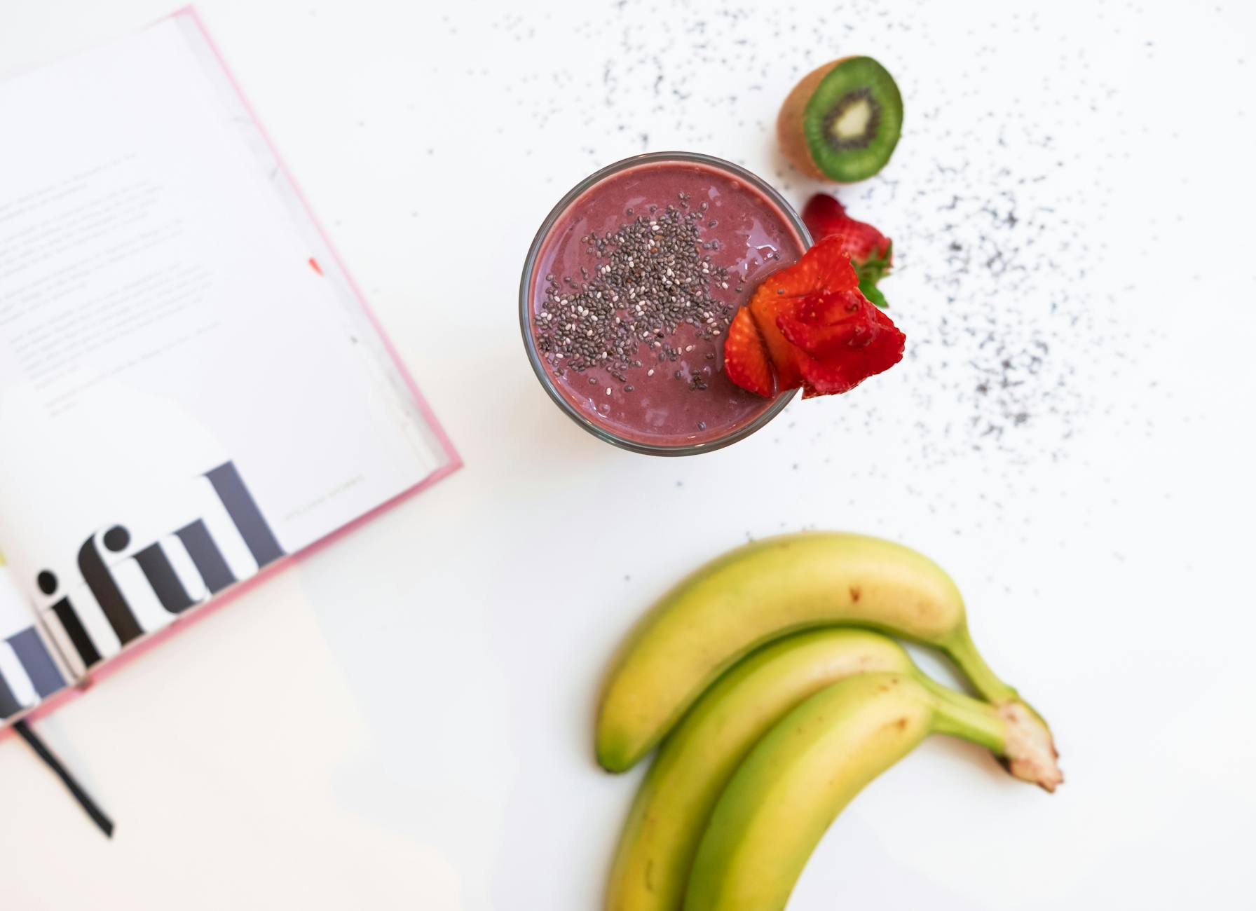 A delicious banana and berry smoothie topped with chia seeds, accompanied by fresh fruits and a magazine. - detox drink recipes