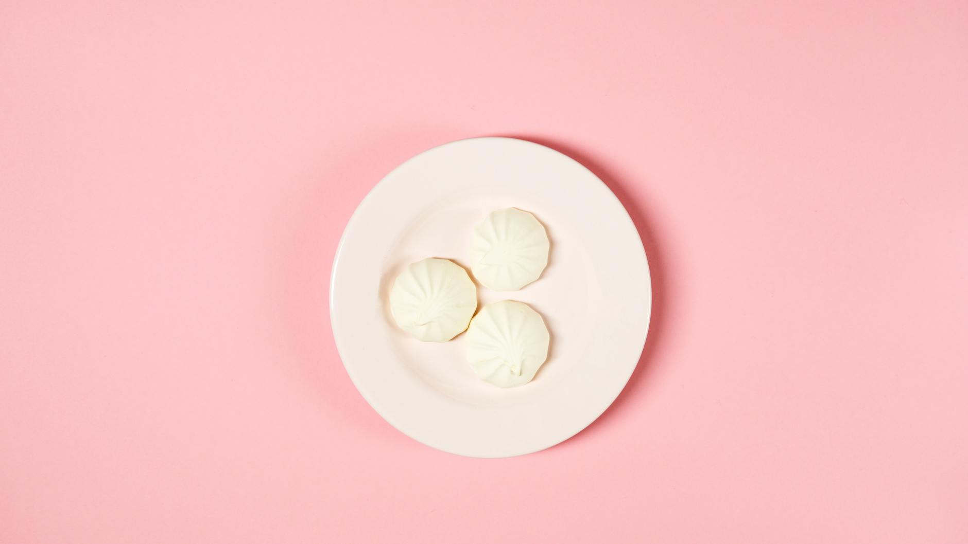 Elegant flatlay of white meringue cookies on a plate with a soft pink background. - diabetic snack ideas
