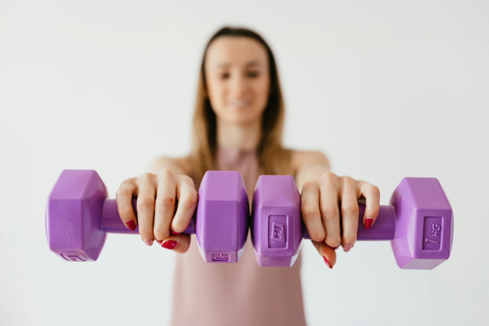 Defocused content young female doing bicep exercise with dumbbells during functional training in light studio - dumbbell workout