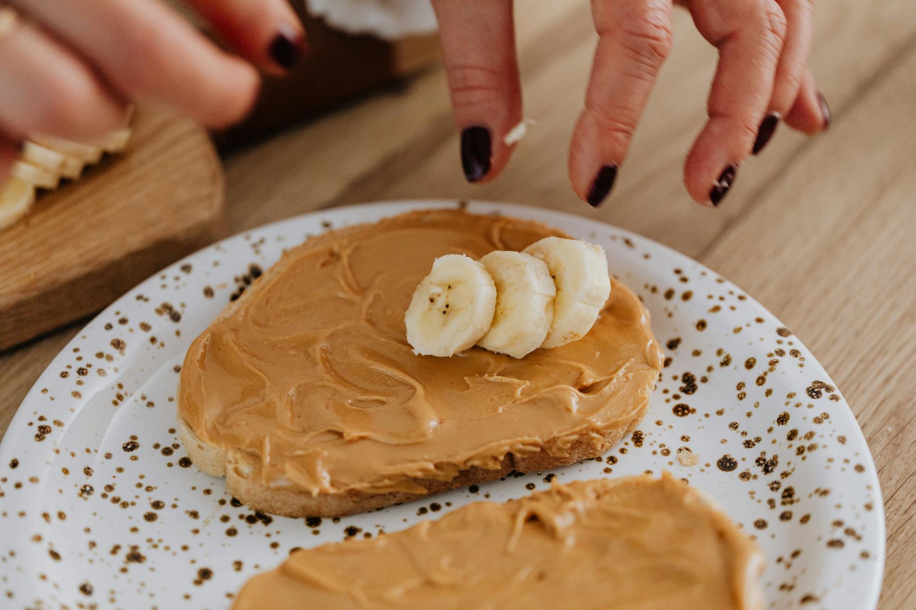 Hands prepare peanut butter banana toast on artistic ceramic plate for healthy breakfast. - easy healthy recipes