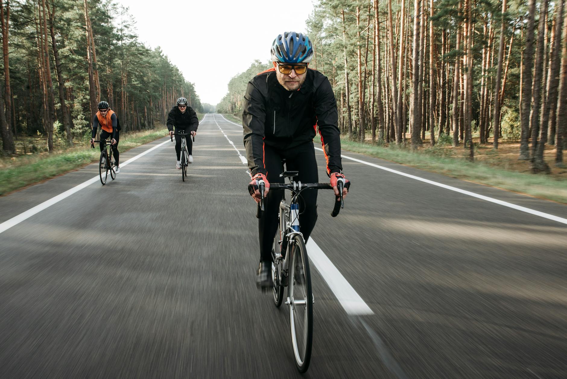 Group of cyclists riding through a forest on a quiet road during the day. - endurance cycling training