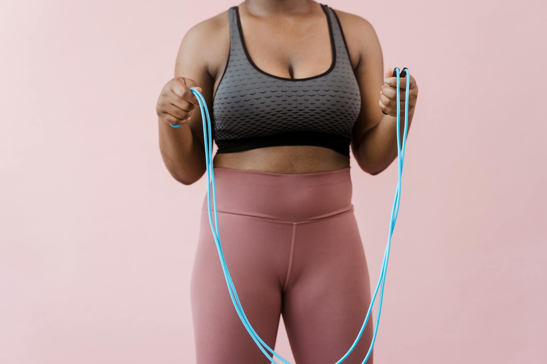 Close-up of a woman in activewear holding a jump rope against a pink background. - no equipment cardio workout