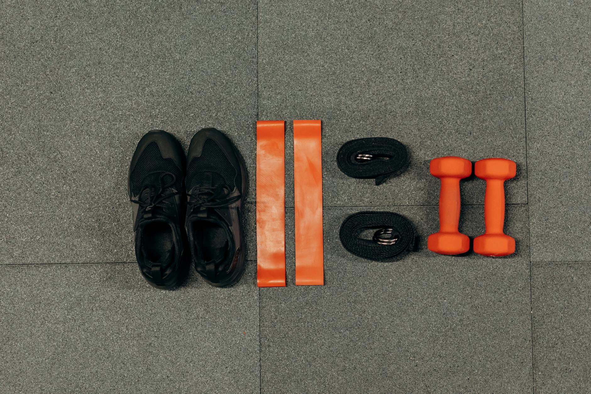 Flat lay of gym essentials including dumbbells, sneakers, and resistance bands on a grey floor. - fitness weight loss plan
