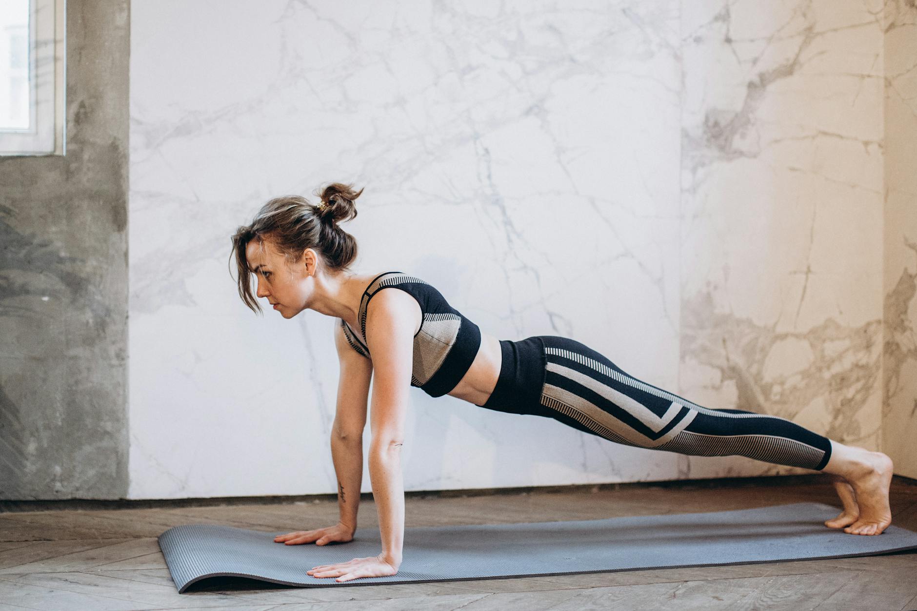 A woman performing a plank pose on a yoga mat indoors, showcasing strength and focus. - flexibility stretching routine
