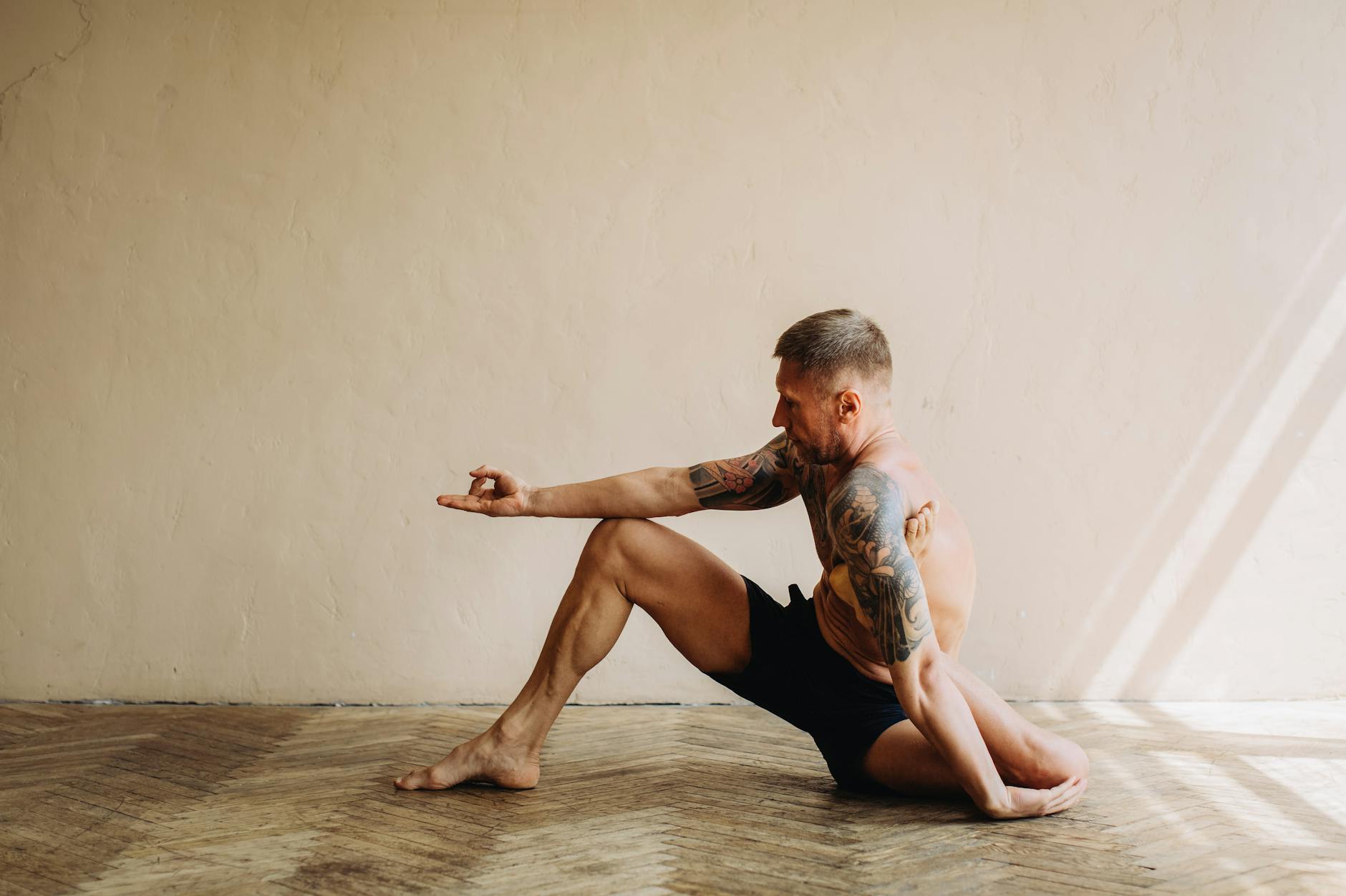Tattooed man performing yoga indoors, showcasing strength and flexibility in a serene setting. - full body stretch