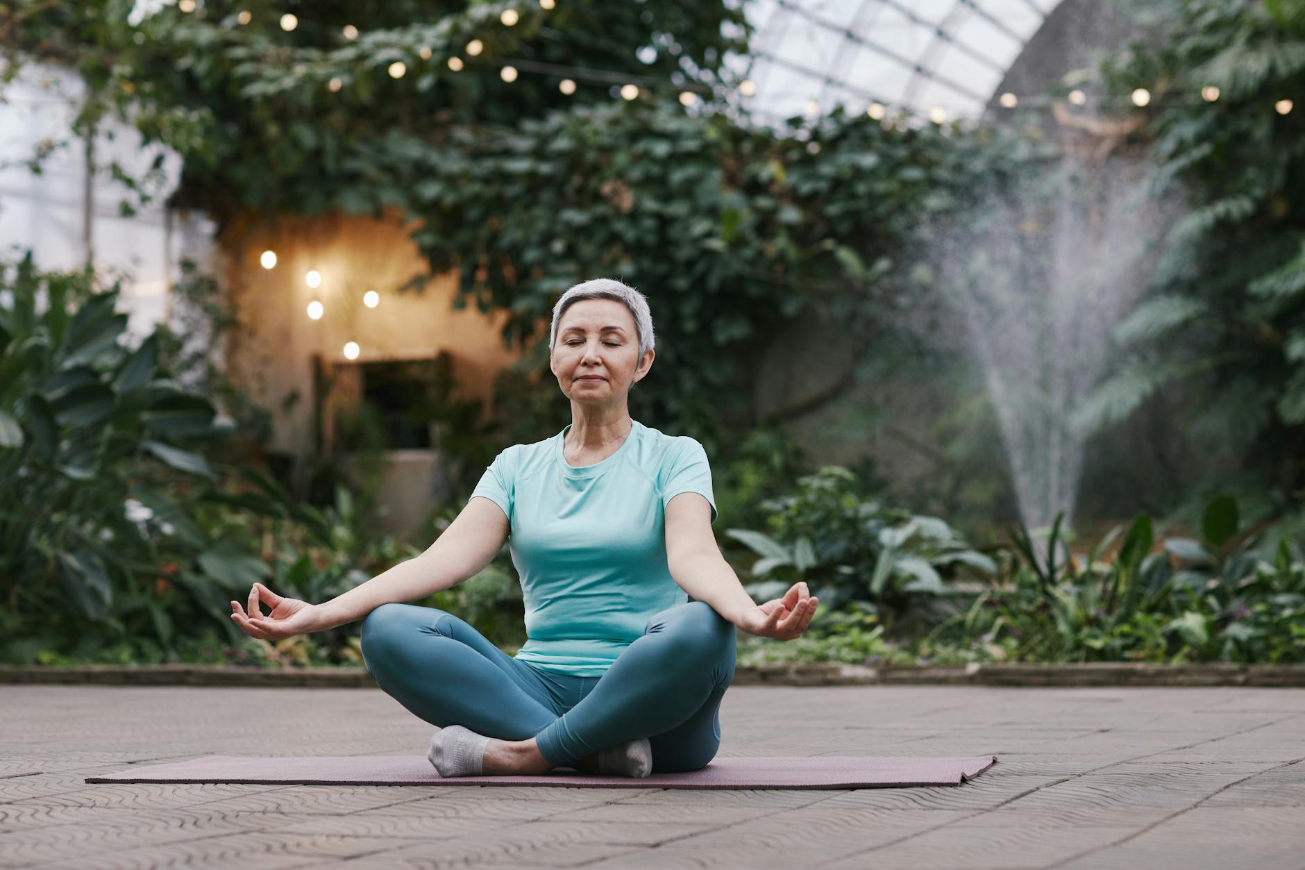 Elderly woman meditating in serene botanical garden setting, focused on wellness and mindfulness. - gardening for exercise