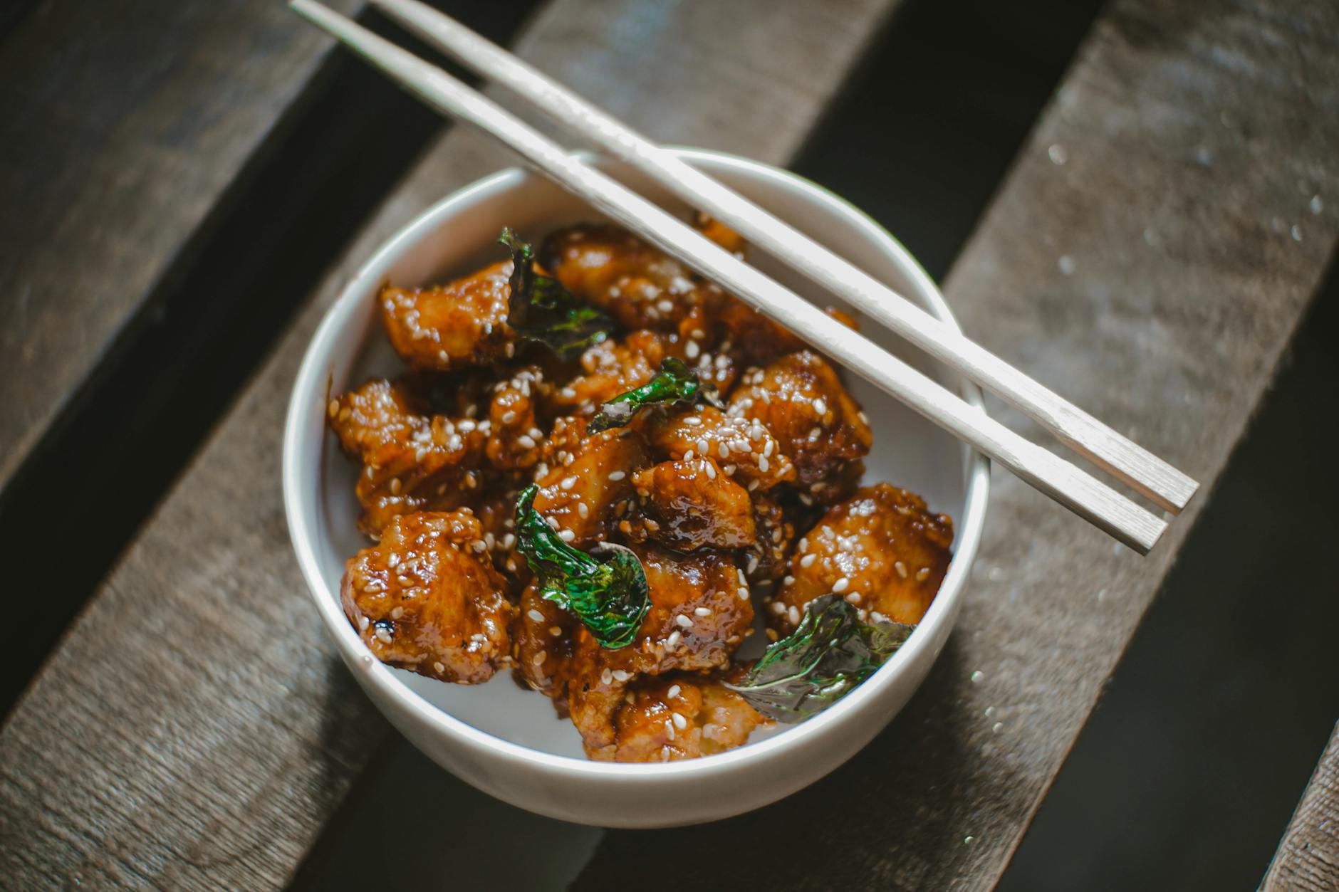 Mouthwatering Korean chicken bowl garnished with sesame seeds and herbs, served with chopsticks. - healthy chicken recipes