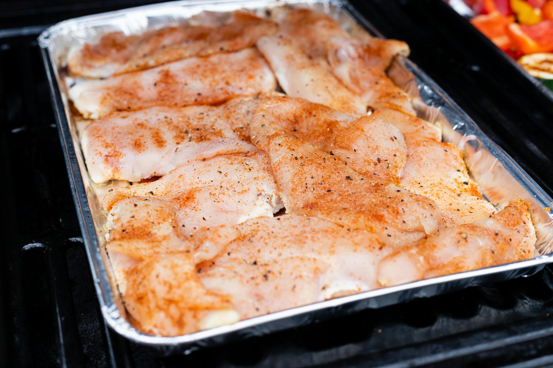 Close-up of seasoned raw chicken breasts in an aluminum tray, ready to cook. - healthy chicken recipes