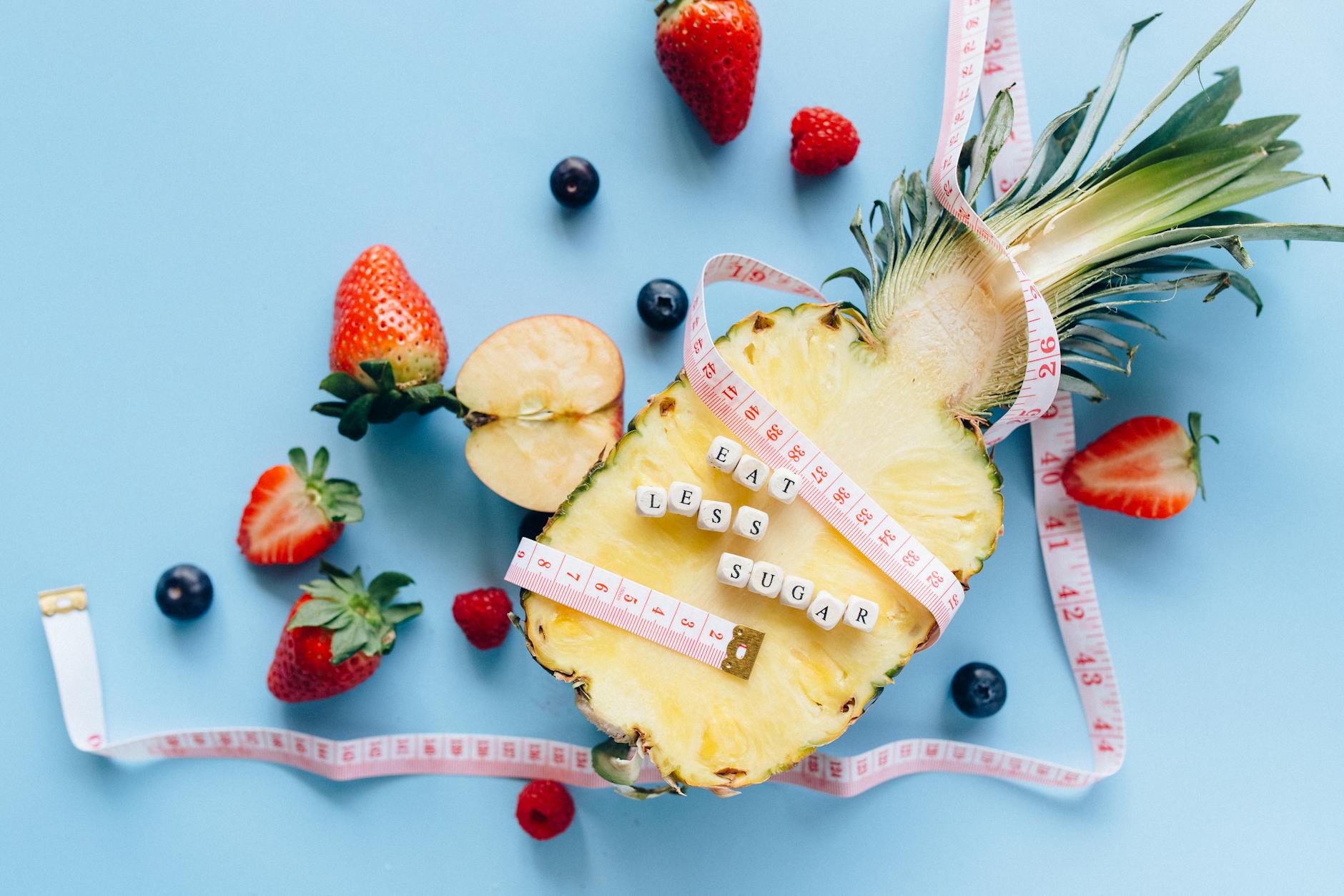 A sliced pineapple with berries and a tape measure on a blue background promoting healthy eating. - healthy diet swaps