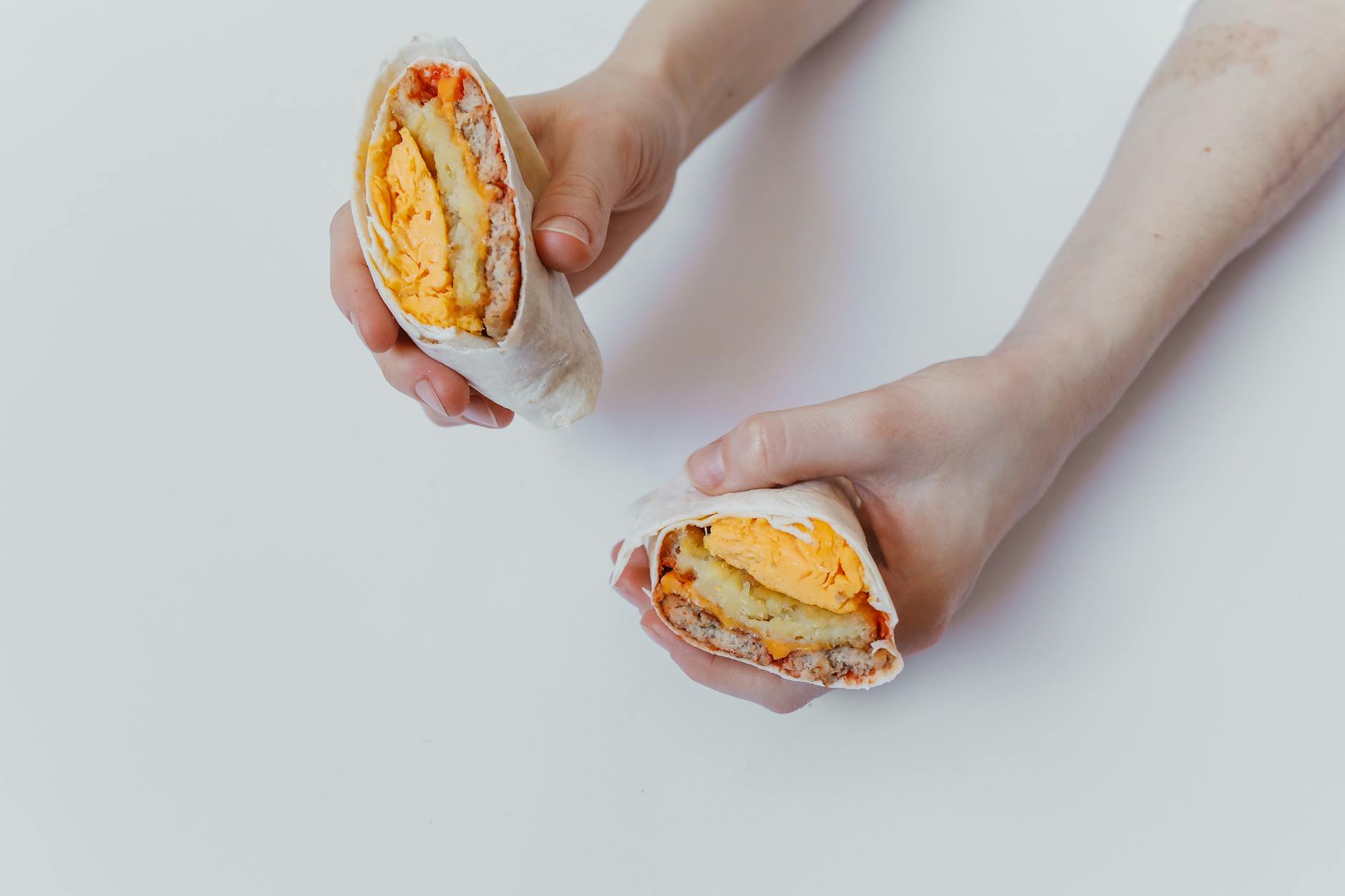 Close-up of hands holding a cut breakfast burrito with eggs, cheese, and meat. - healthy fast food breakfast