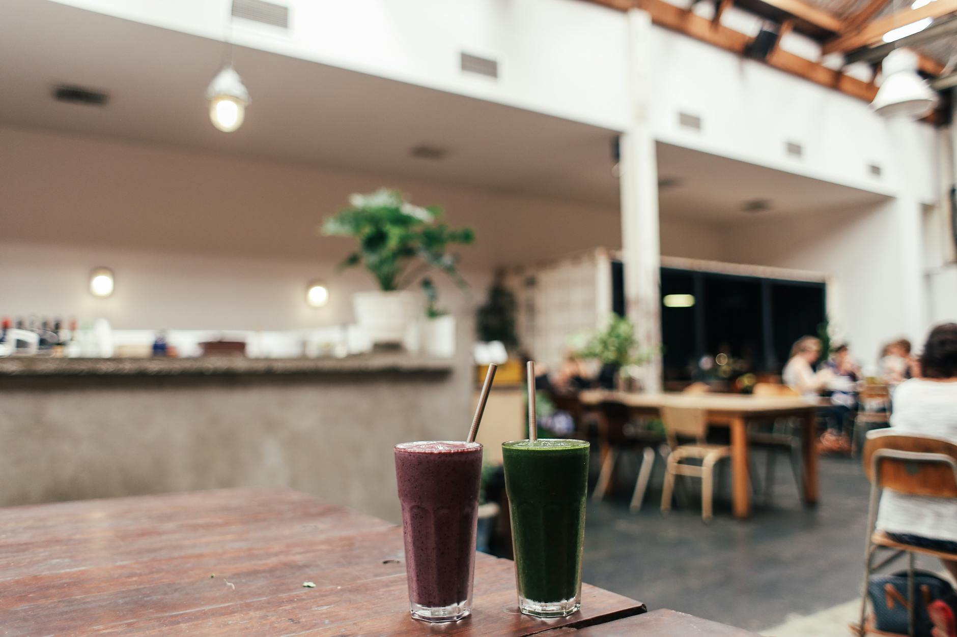 Two fruit smoothies on a wooden table in a modern café interior setting. - healthy green smoothie