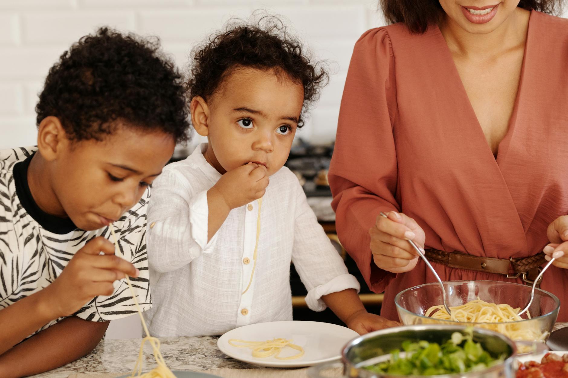 Mother and children eating spaghetti indoors at home kitchen. - healthy kid meals