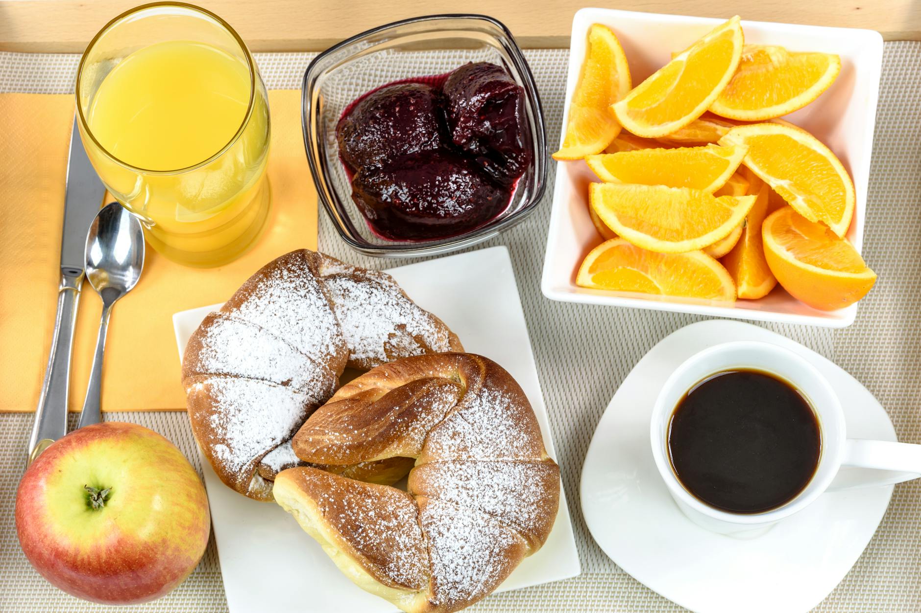 Fresh continental breakfast with croissant, coffee, orange slices, juice, jam, and apple, served on a plate. - healthy mcdonalds breakfast
