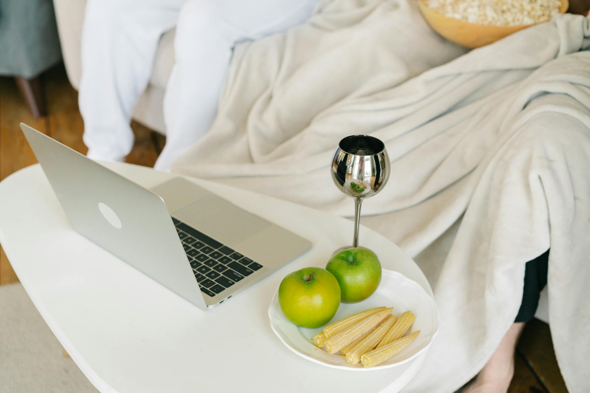 A relaxing indoor setup featuring a laptop, green apples, baby corns, and a decorative cup. - healthy office snacks