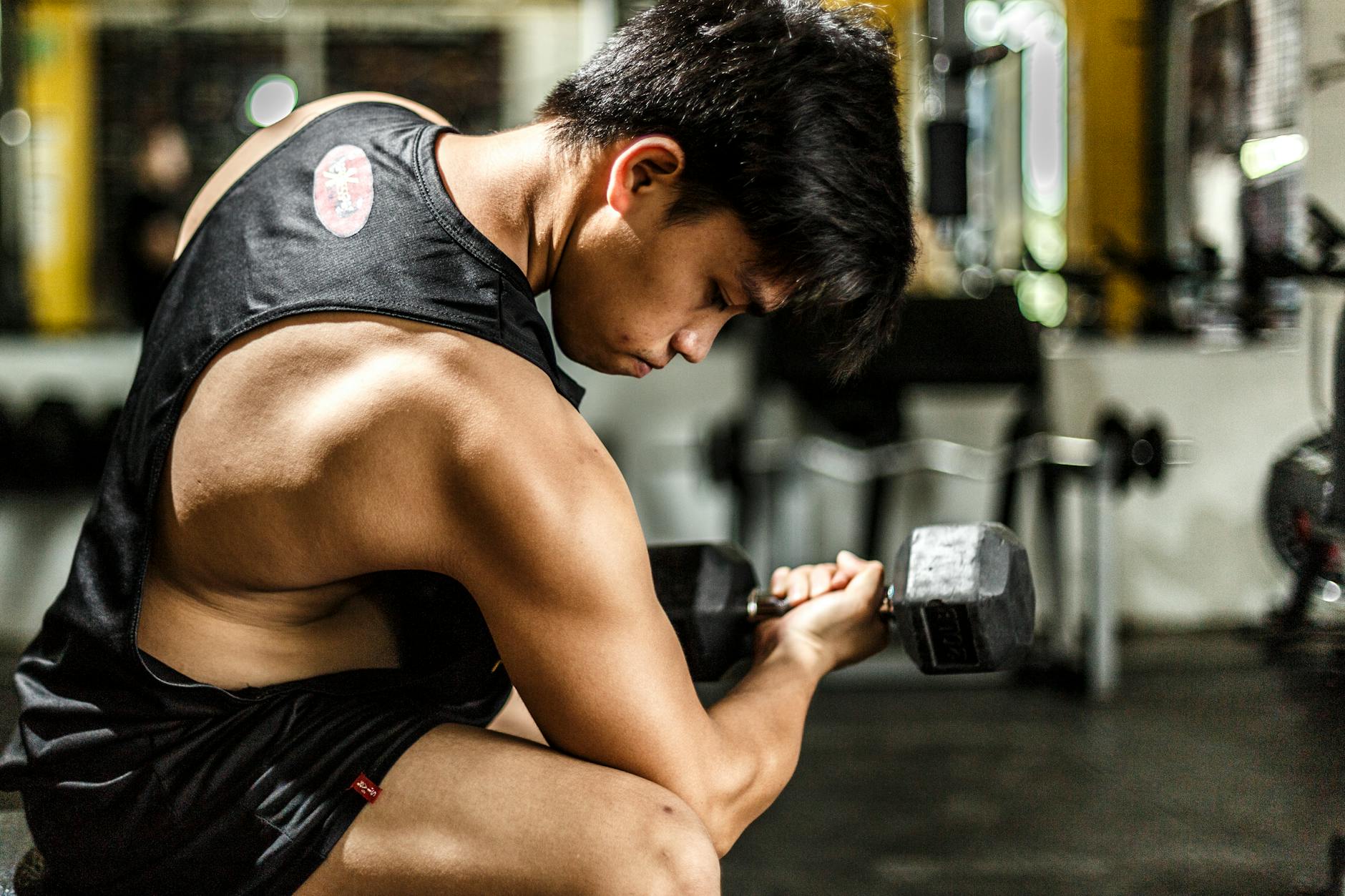 Young man intensely lifting a dumbbell in a gym, highlighting strength and focus. - high intensity interval training