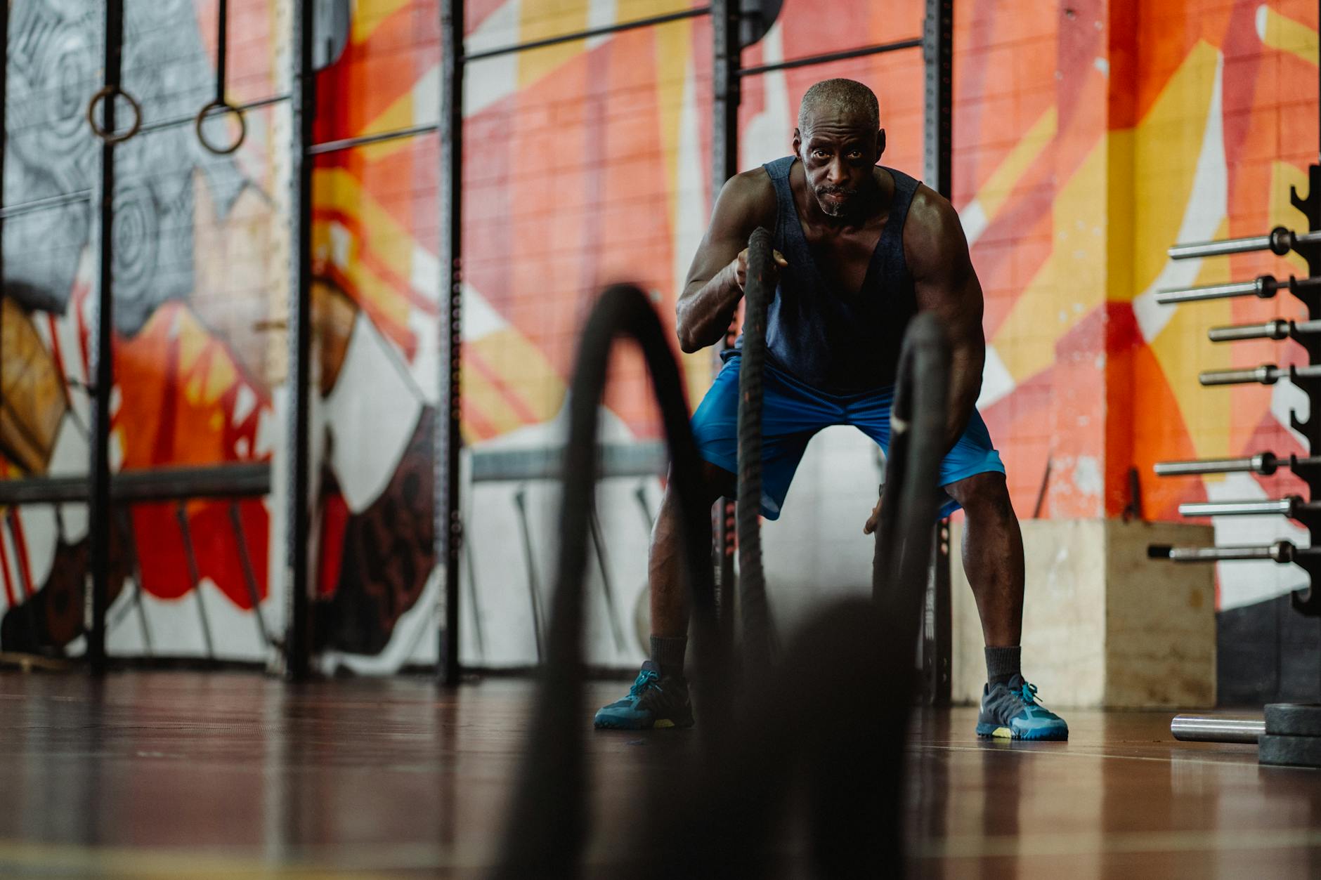 A focused man exercises with battle ropes in a colorful gym mural setting. Strength and energy exude. - high intensity interval training