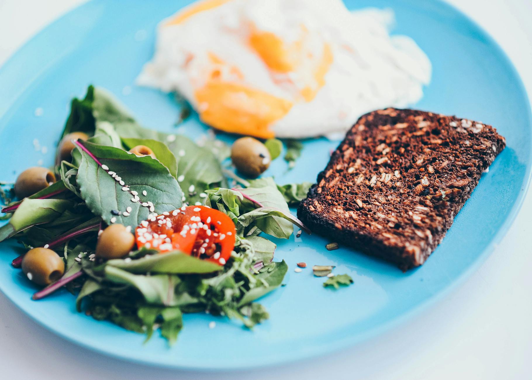 A nutritious breakfast plate featuring eggs, rye bread, salad, and olives on a vibrant blue plate. - high protein breakfast ideas