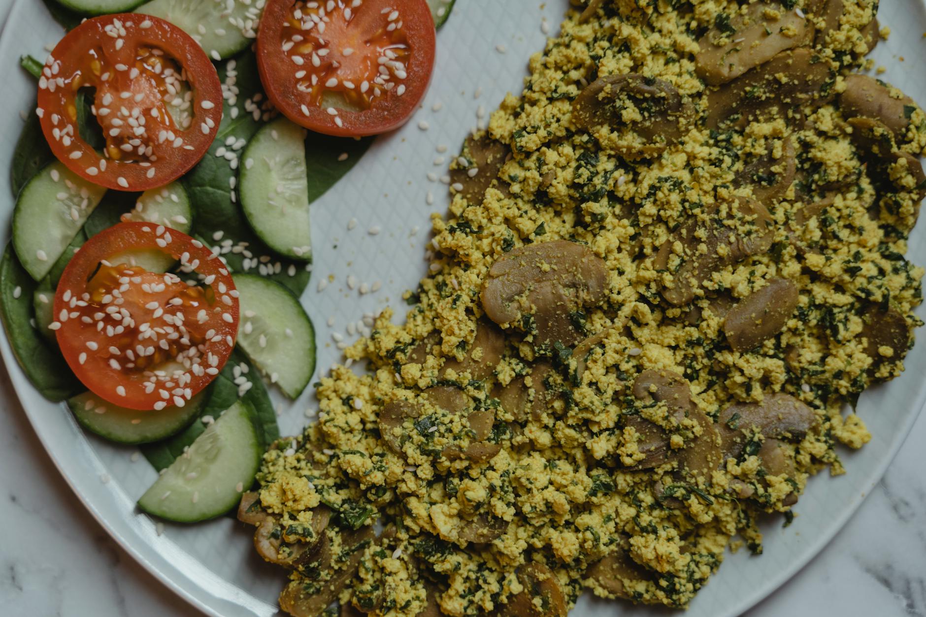 Healthy vegan meal with tofu scramble, cucumbers, and tomatoes on a marble surface. - high protein low carb