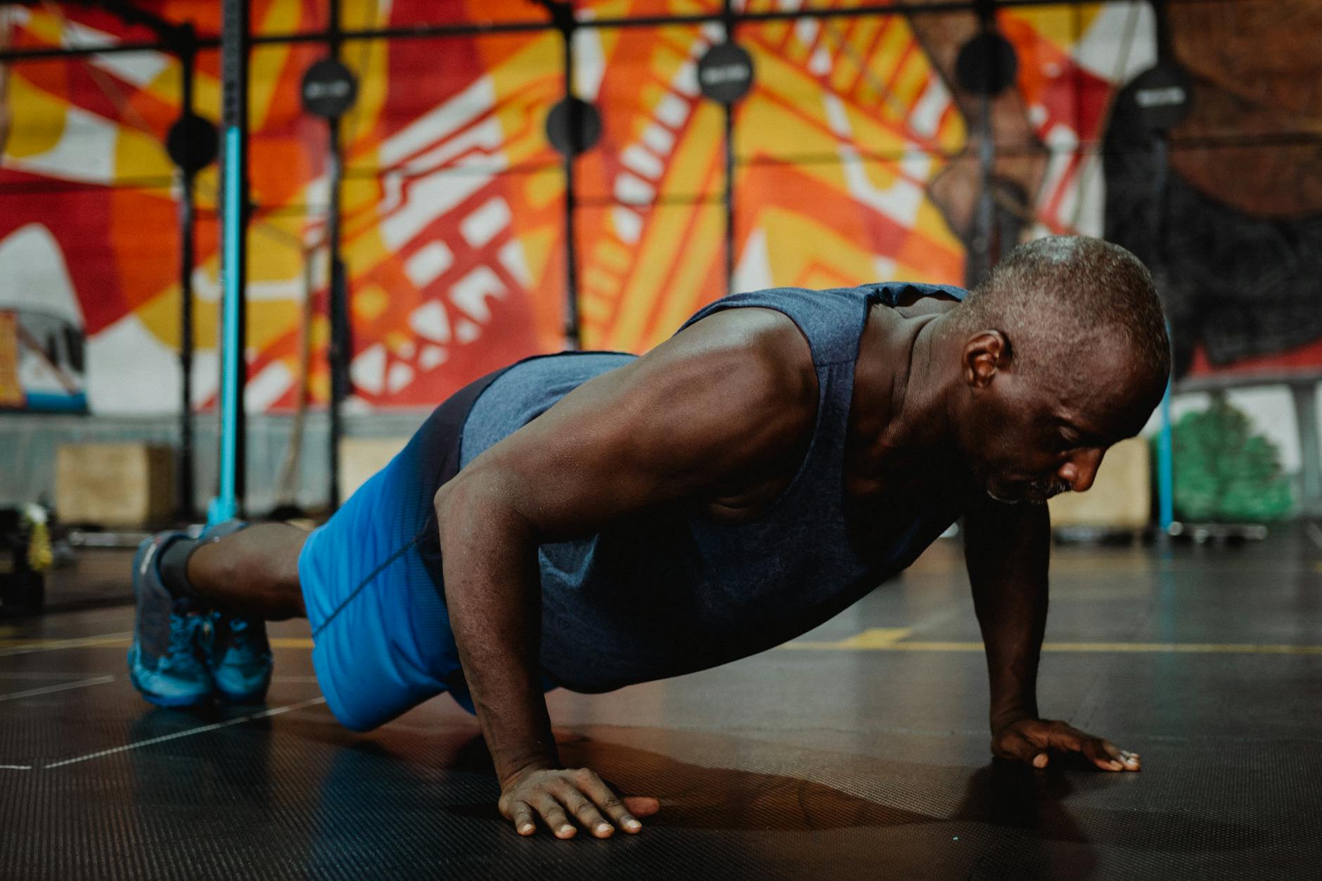 Adult man doing push-ups in a colorful gym setting, promoting fitness and health. - what is hiit