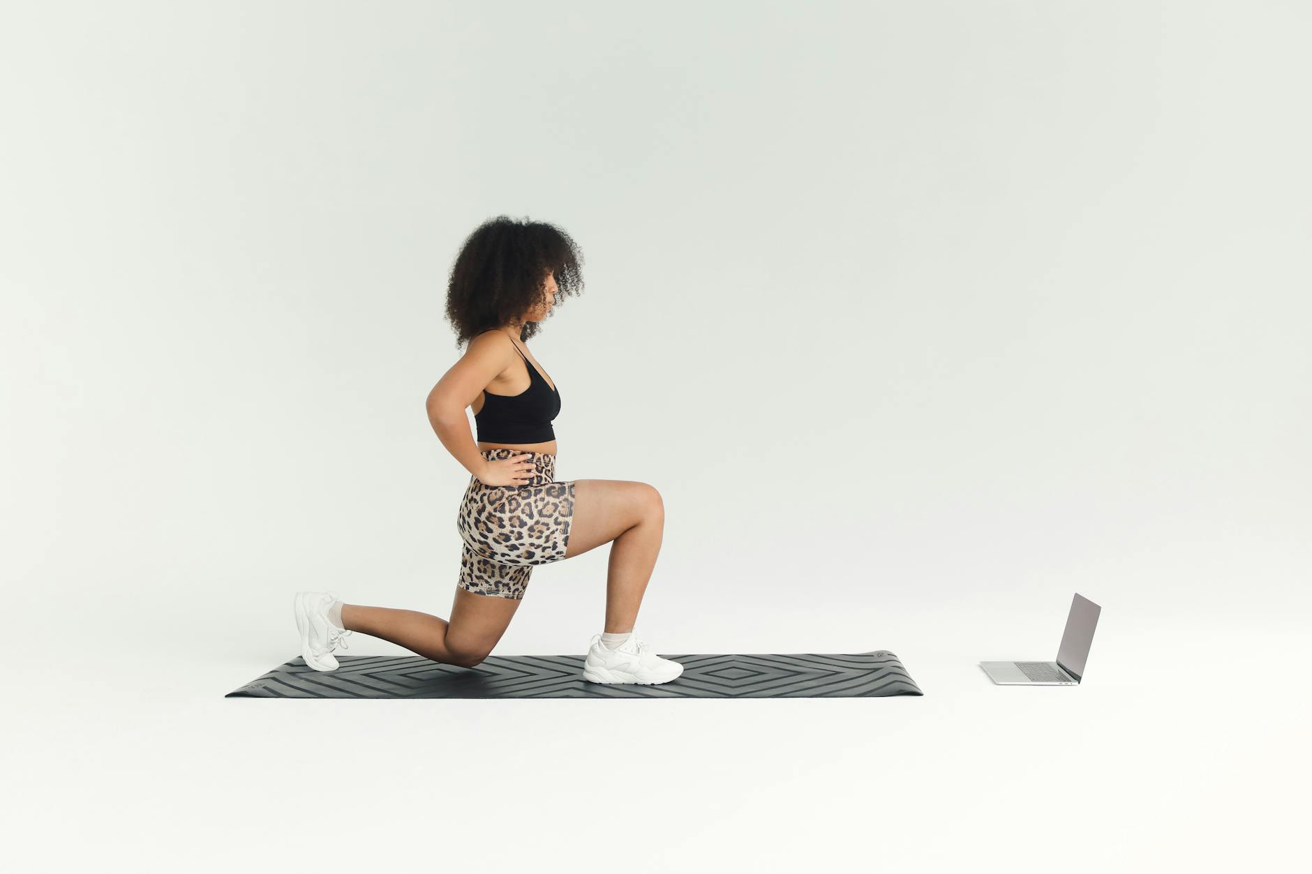 A woman doing a lunge exercise indoors with a laptop for guidance. - hiit cardio workout