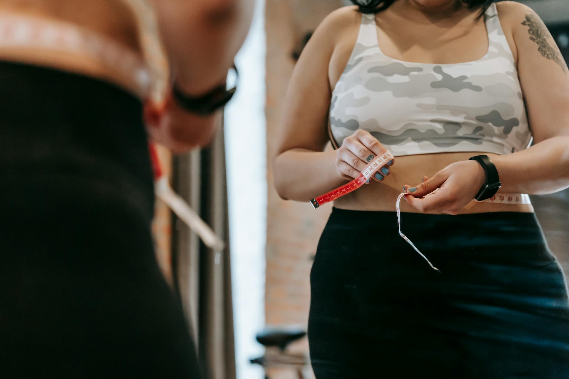 Woman in sportswear measuring her waist with a tape measure, emphasizing fitness and body awareness. - hiit fat loss