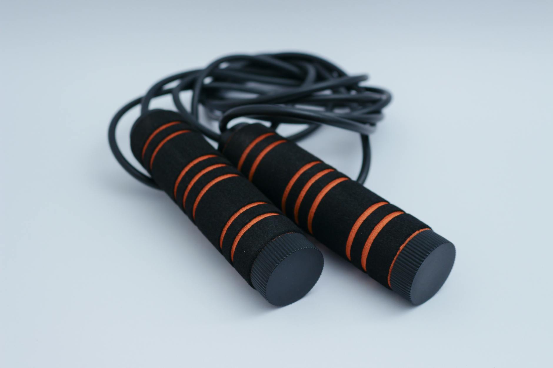 A minimalist close-up of black and orange exercise skipping rope on a clean white background. - home cardio workout