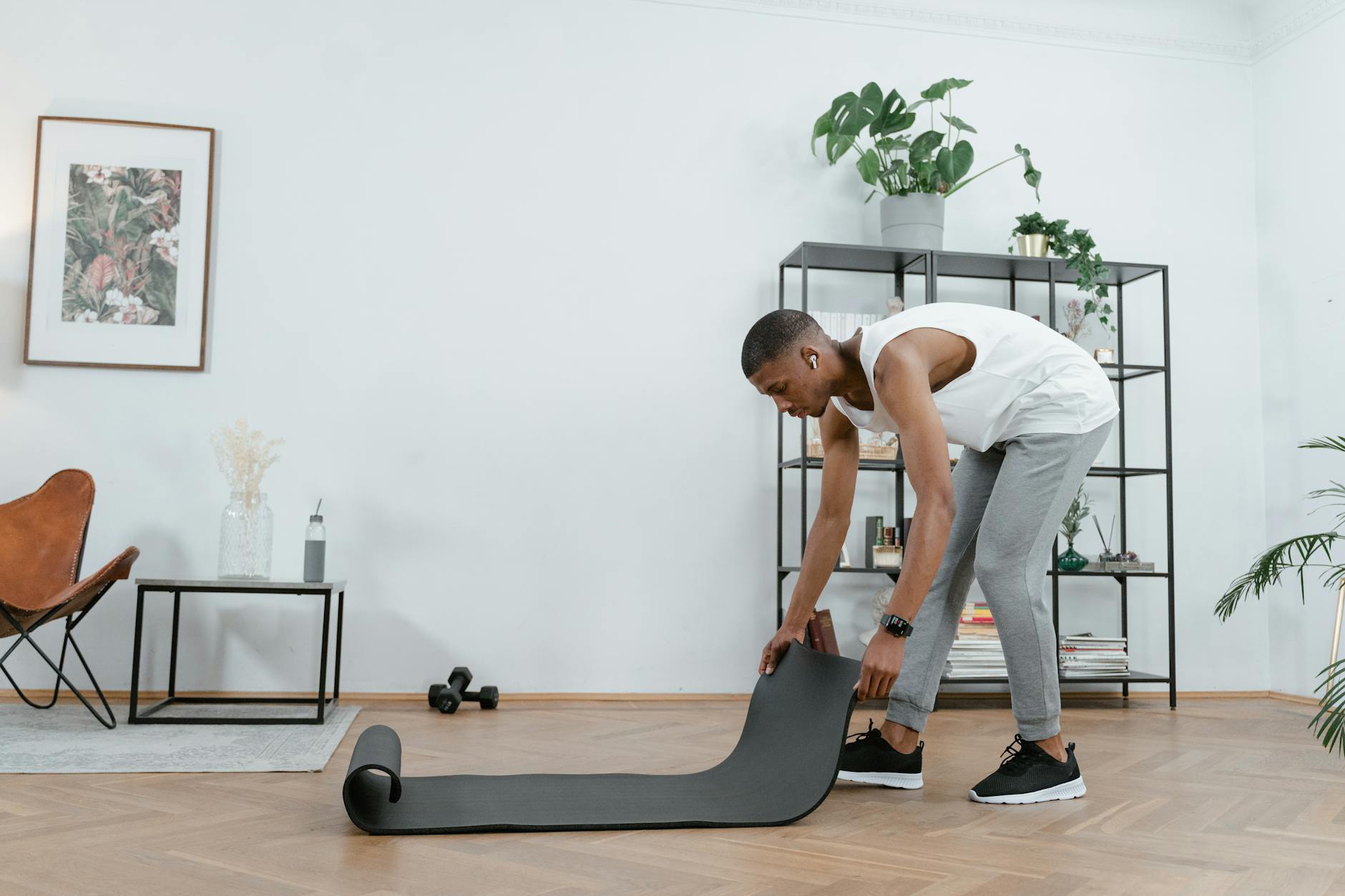 A young man setting up a yoga mat in a stylish home interior for a workout session. - home workout plan
