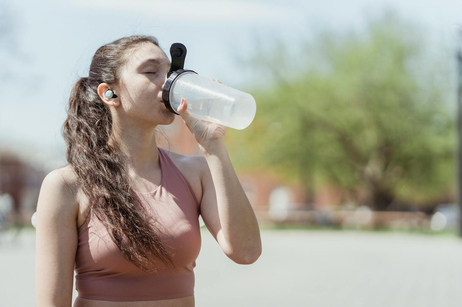 Young woman in sportswear drinks water outdoors, enjoying a sunny day. - hydration hacks