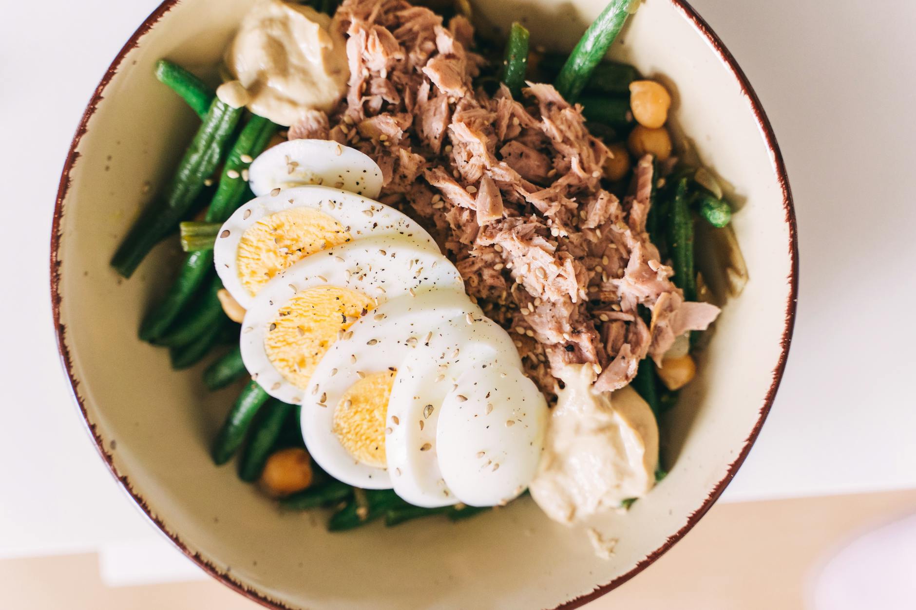 Delicious protein-packed bowl featuring tuna, boiled eggs, green beans, and hummus. - iron protein foods