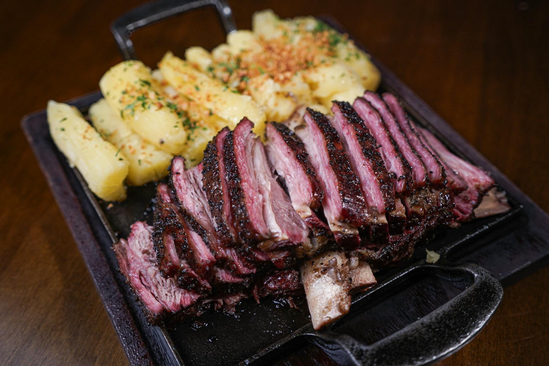 Juicy grilled beef ribs served with seasoned potatoes on a sizzling iron skillet, perfect for a hearty meal. - iron rich foods