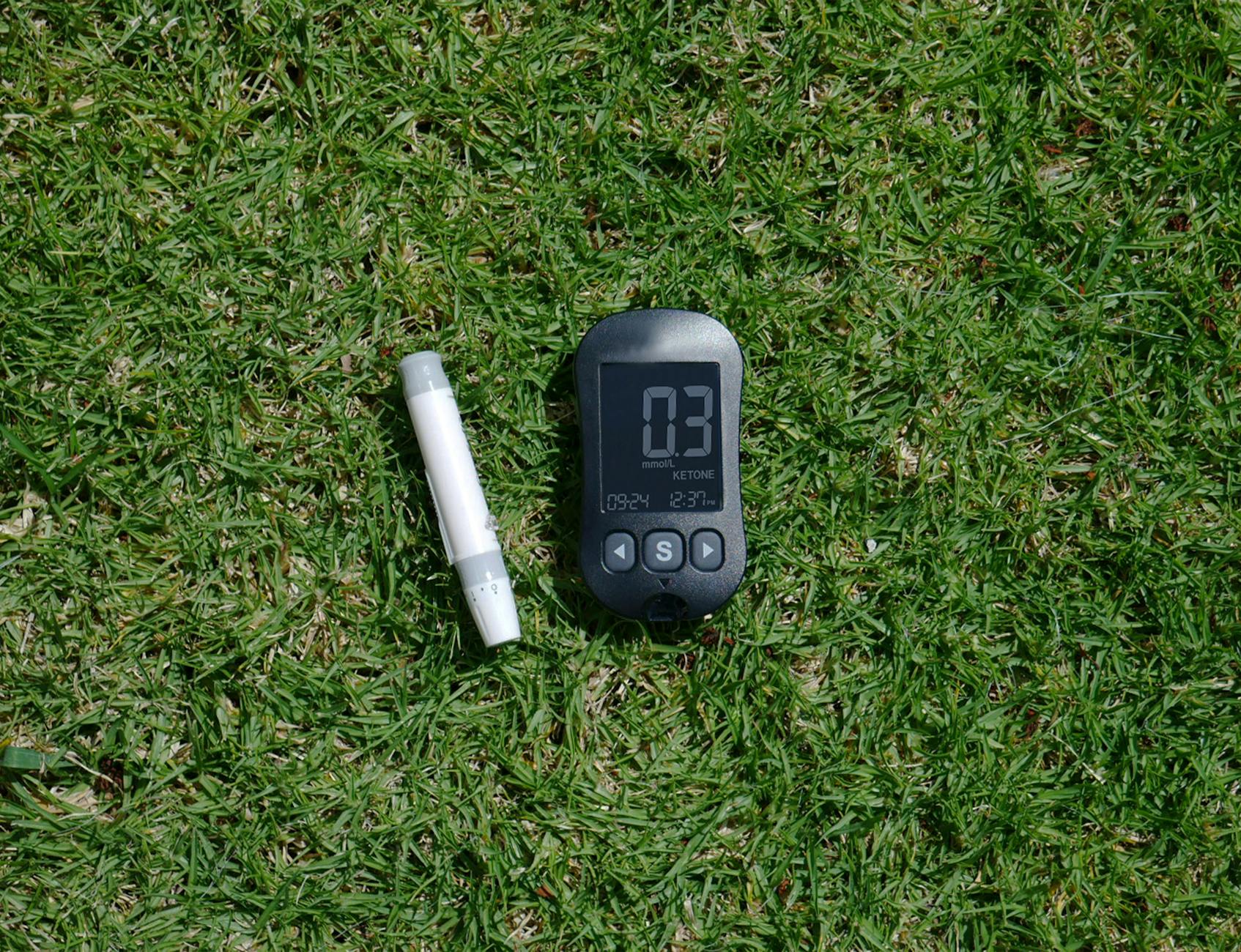 Blood ketone meter and strip displayed outdoors on grass. - what is keto diet