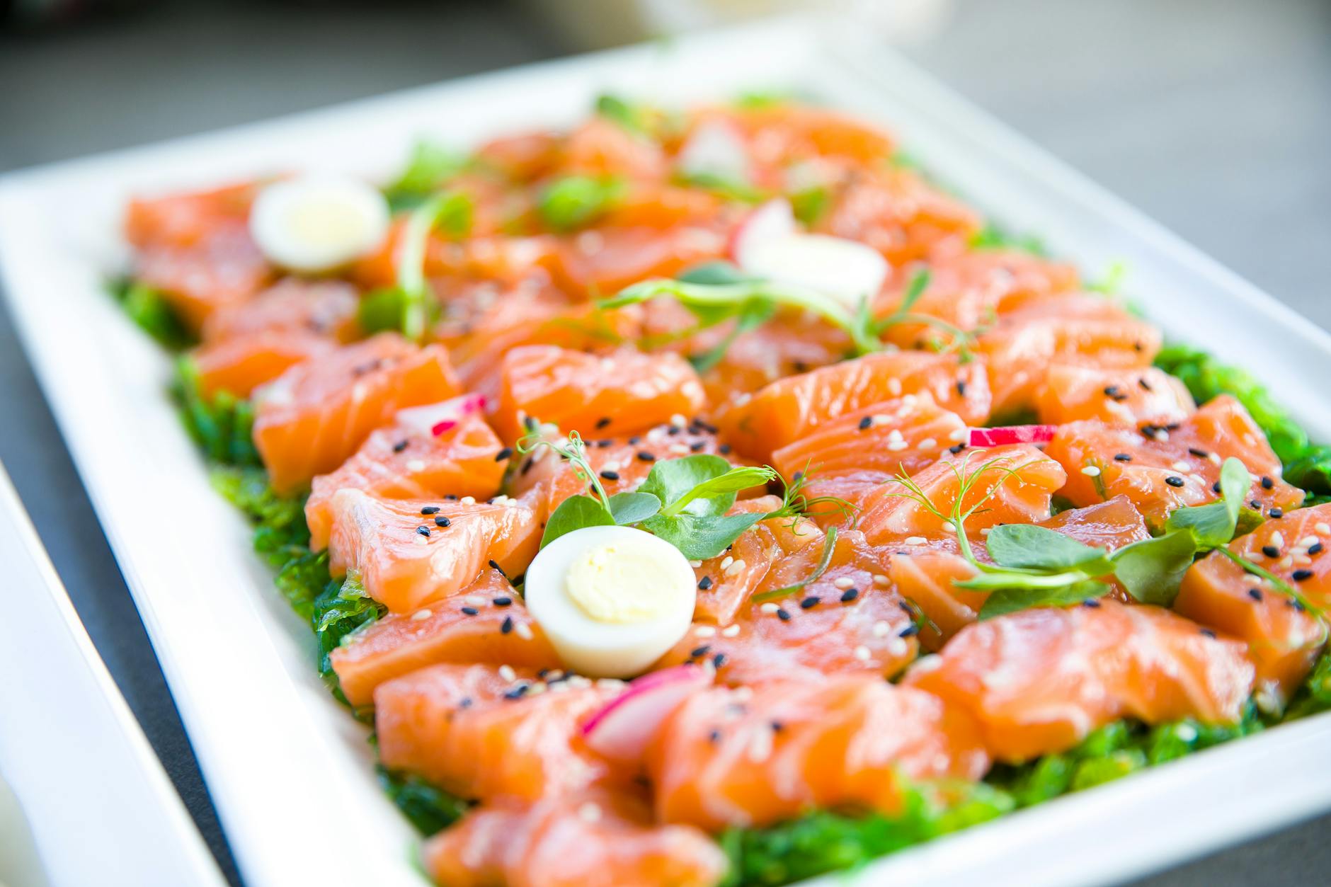 Delicious salmon sashimi garnished with quail eggs and fresh greens on a platter. - keto meal plan