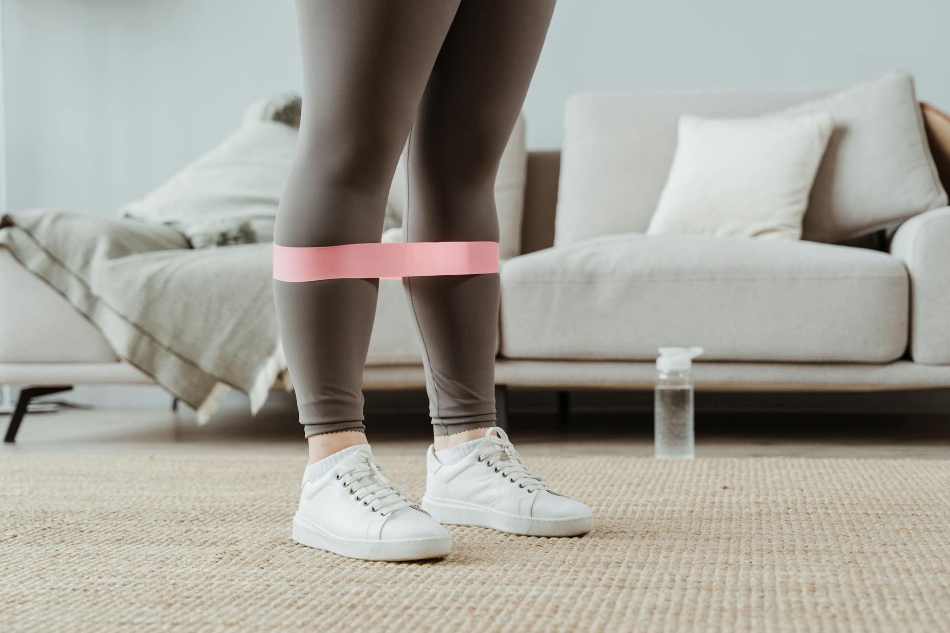 Close-up of a woman in sport leggings using a pink resistance band for leg exercises indoors. - leg workout routine