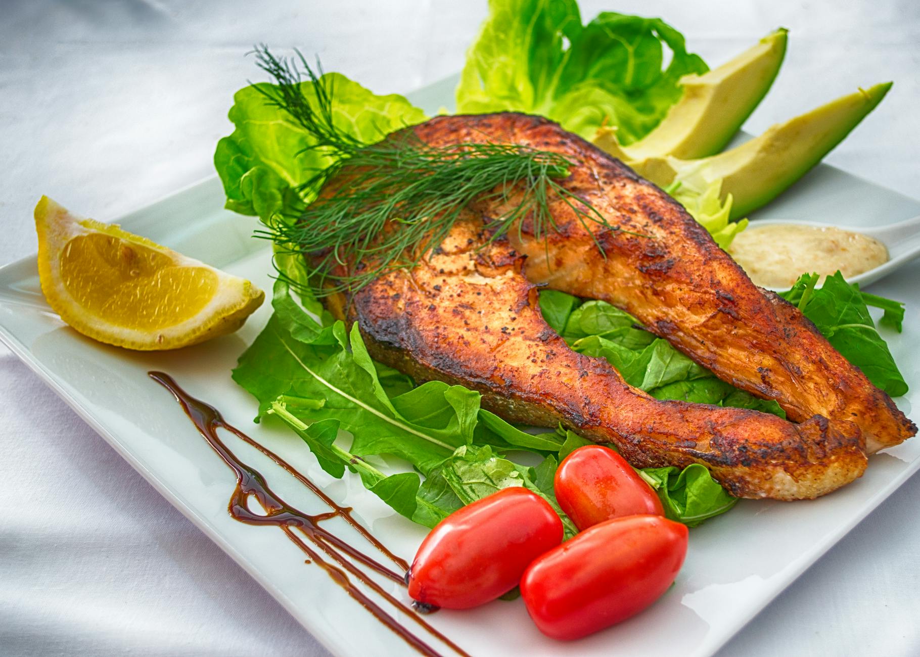 Delicious grilled salmon served with fresh vegetables and herbs on a white plate. - low carb diet