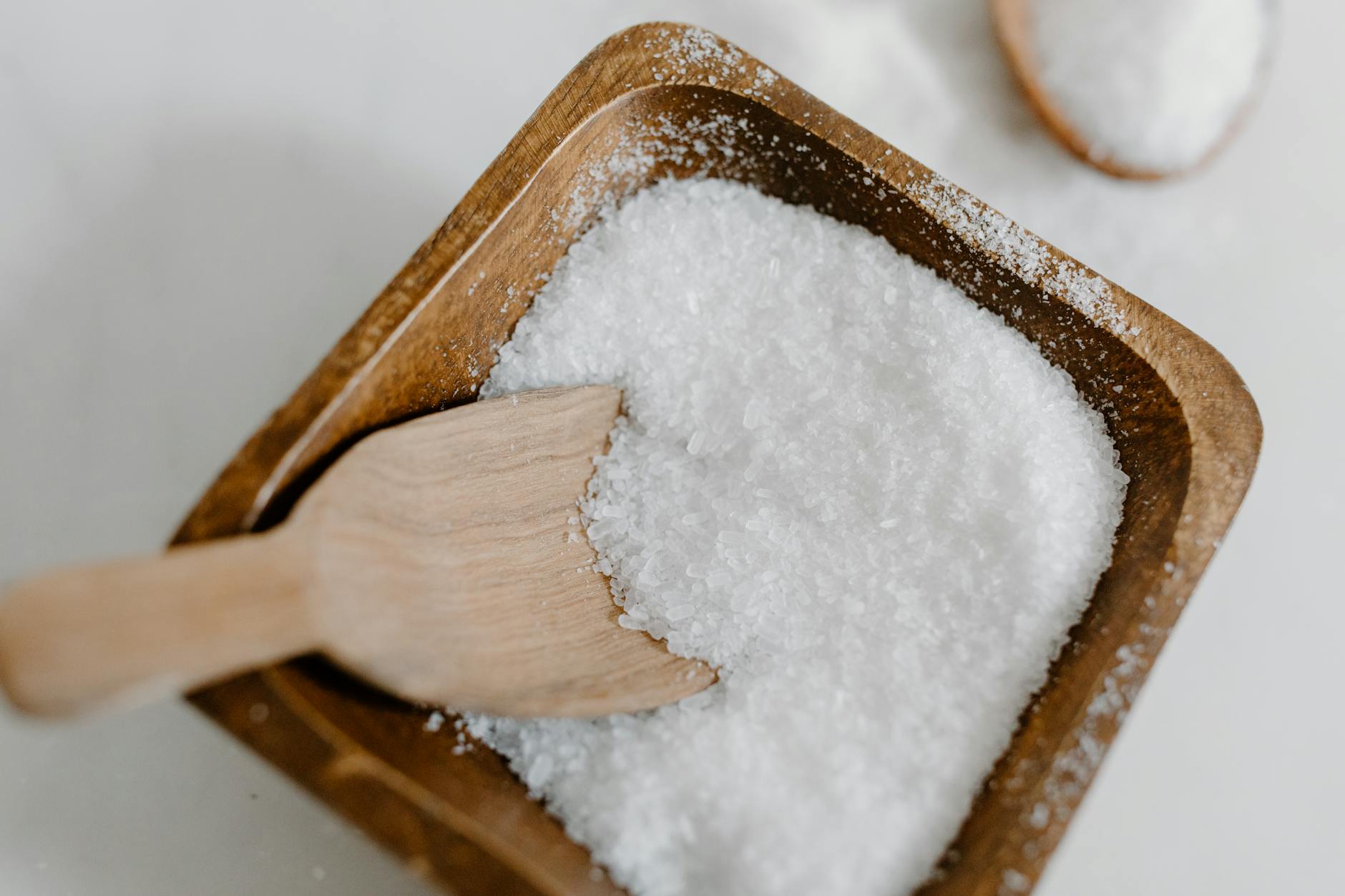 Close-up of coarse sea salt in a wooden bowl with a wooden scoop, perfect for culinary use. - magnesium oxide benefits