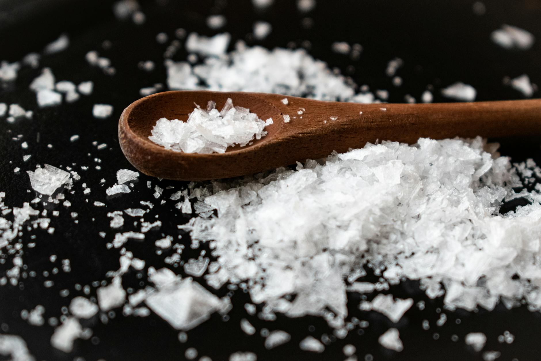Closeup of wooden spoon arranged with sea salt scattered on table in kitchen - magnesium oxide benefits
