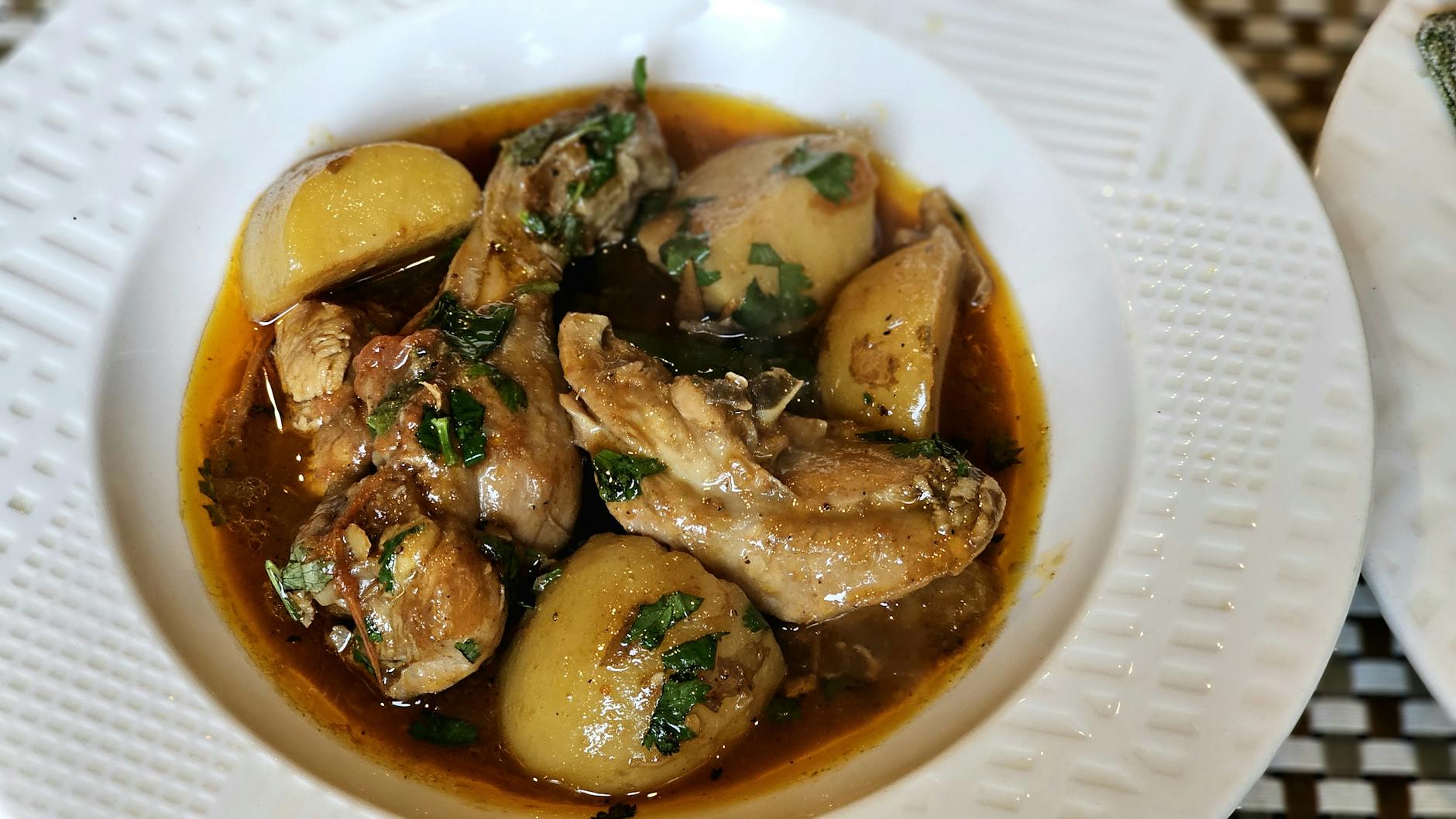 Delicious chicken stew with potatoes, garnished with fresh herbs, served in a white dish. - mediterranean chicken recipe