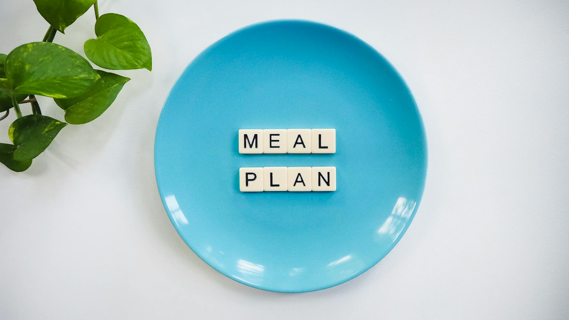 Innovative meal planning concept using alphabet tiles on a blue plate with green leaves. - mediterranean diet plan