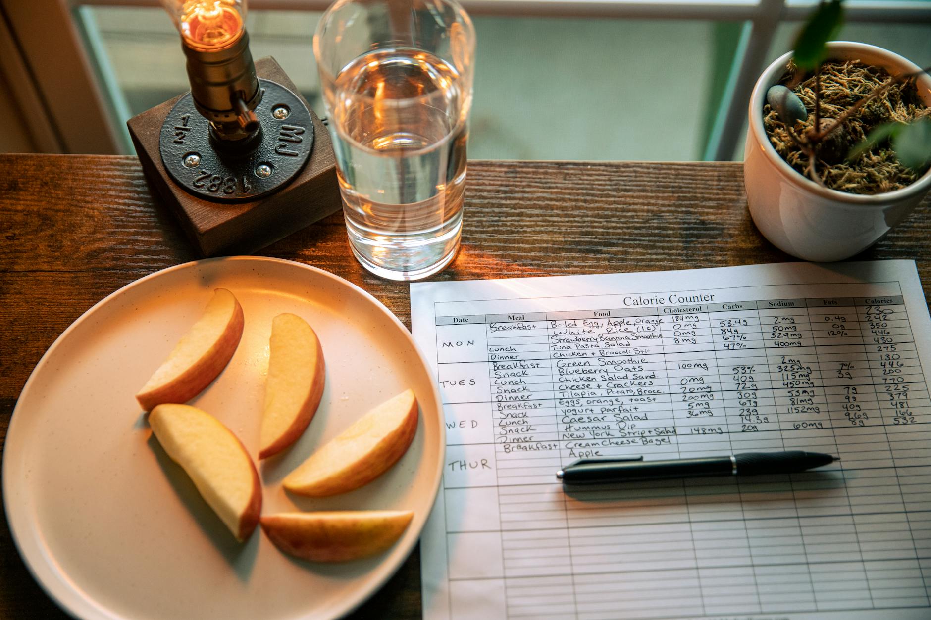 A wooden table setup with apple slices, a calorie chart, and a glass of water for a healthy diet plan. - mediterranean diet plan