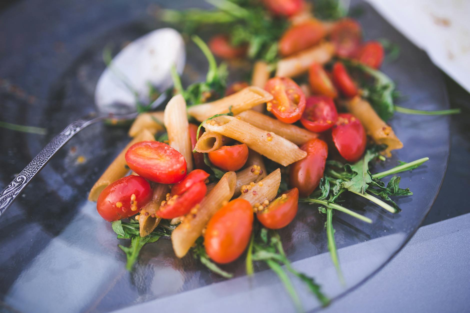 Fresh penne pasta salad with cherry tomatoes and arugula on a glass plate. - mediterranean salad recipe