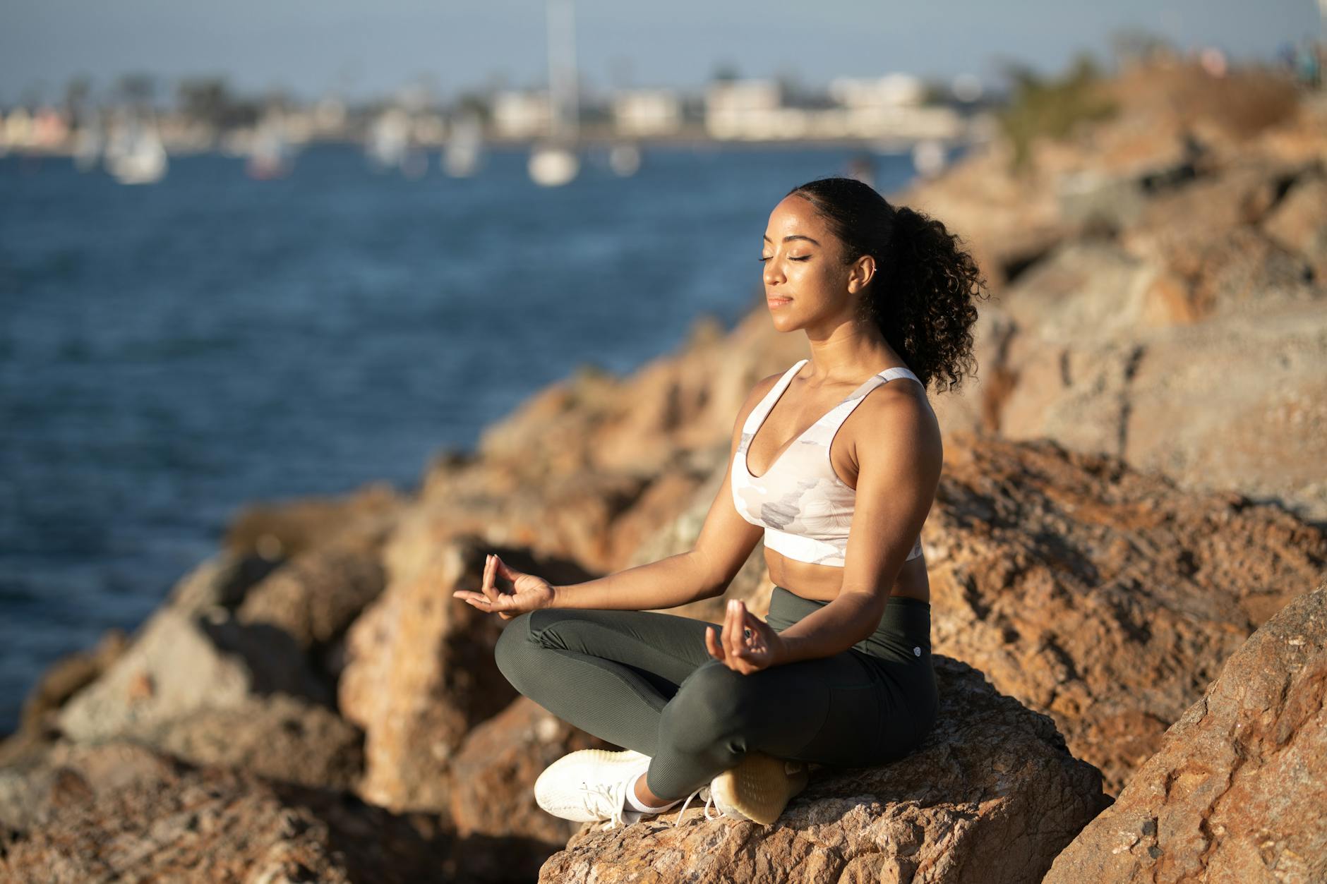 Woman meditating on rocks by the ocean, embodying calmness and wellness. - mindfulness meditation benefits