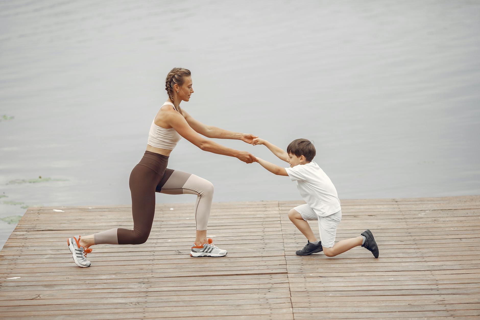 A woman and a boy exercise together on a wooden deck by the lake, promoting healthy lifestyle. - morning exercise kids
