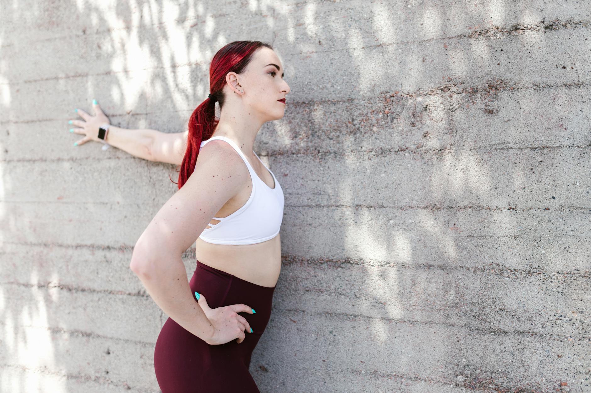 Fitness woman stretching against a sunlit concrete wall wearing activewear. - morning stretch routine