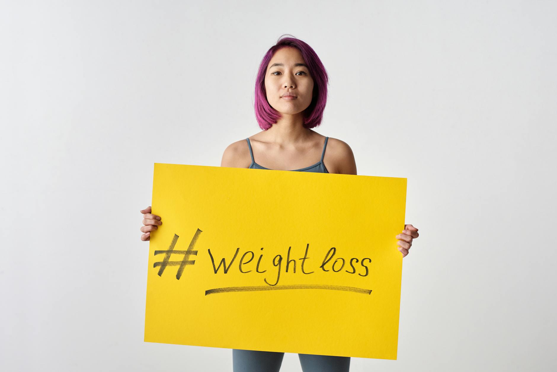 Asian woman with purple hair holding a weight loss sign in a studio setting. - natural weight loss
