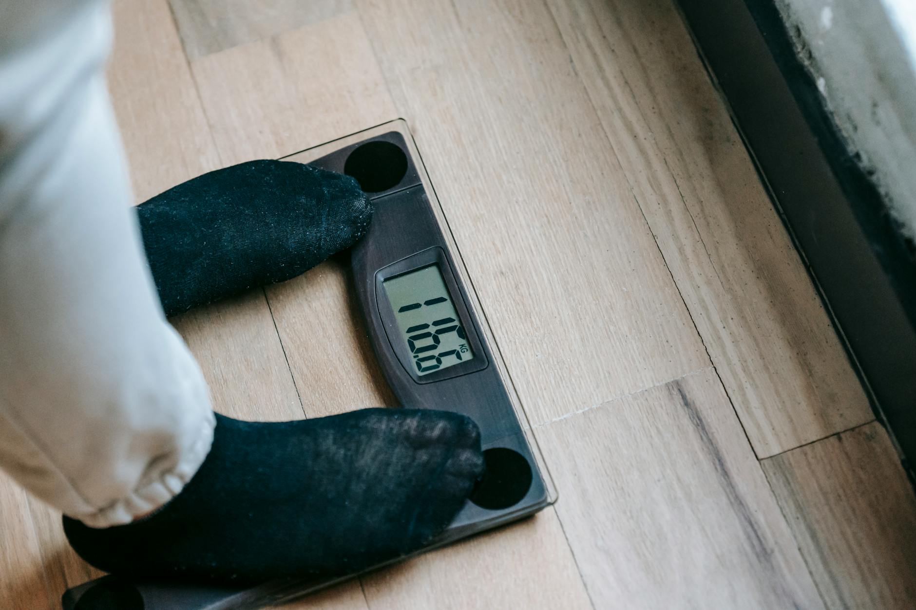 From above of unrecognizable person in socks standing on electronic weighing scales while checking weight on parquet during weight loss - natural weight loss