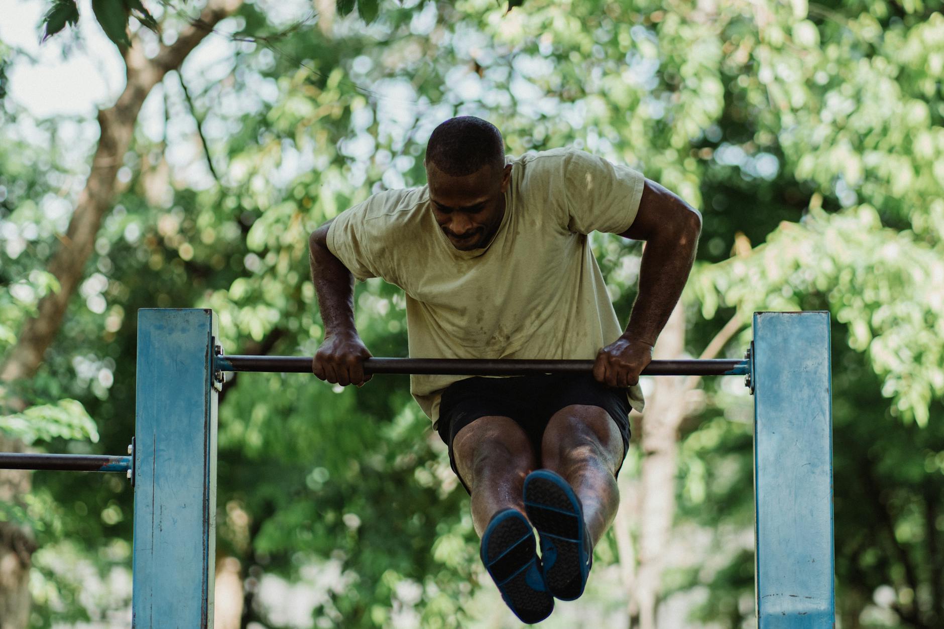 A fit man doing a pull-up on an outdoor bar in a sunny park, showcasing strength and fitness. - neck posture exercises