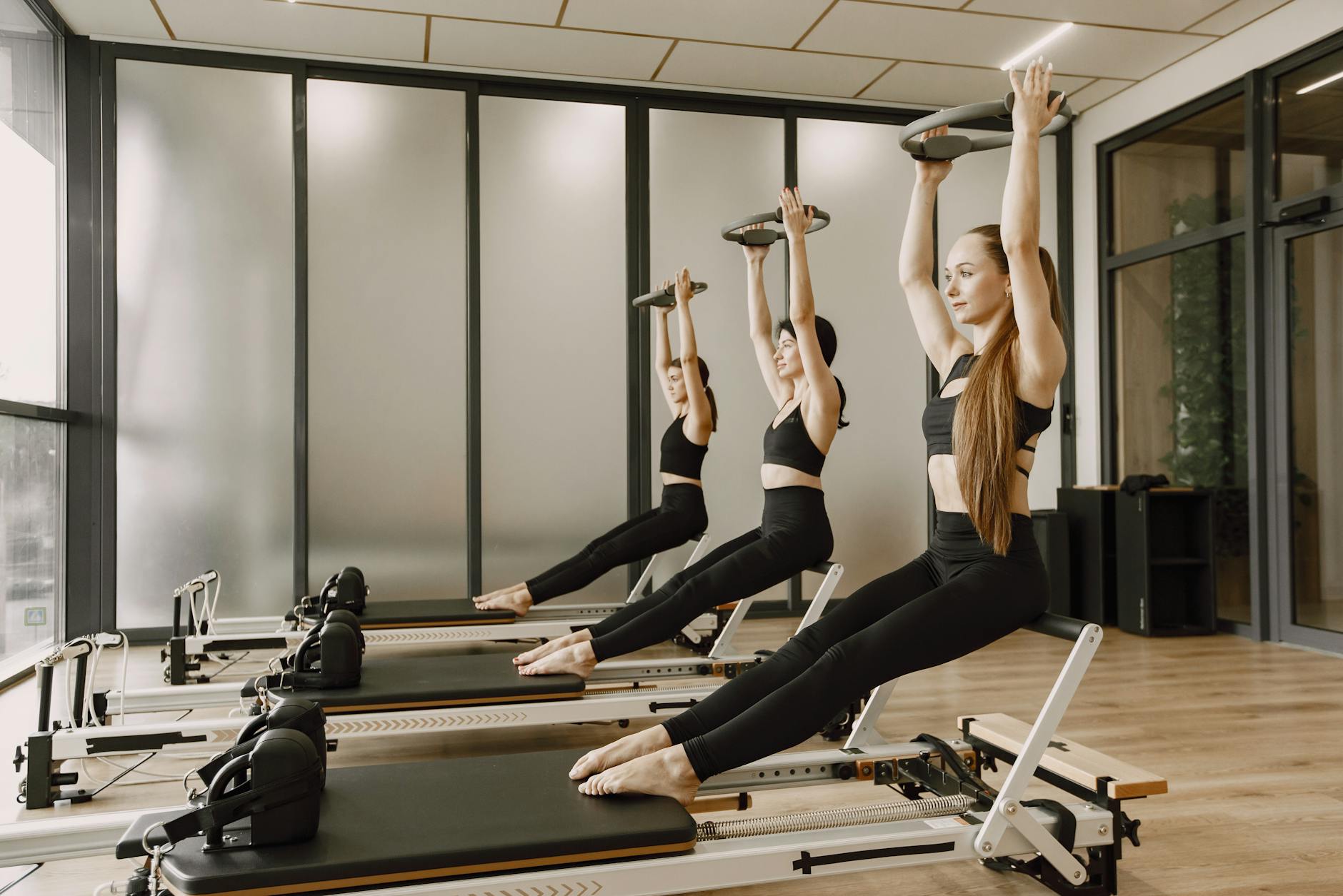 Three women synchronously practicing Pilates on reformers in a modern gym studio. - pilates chair exercises