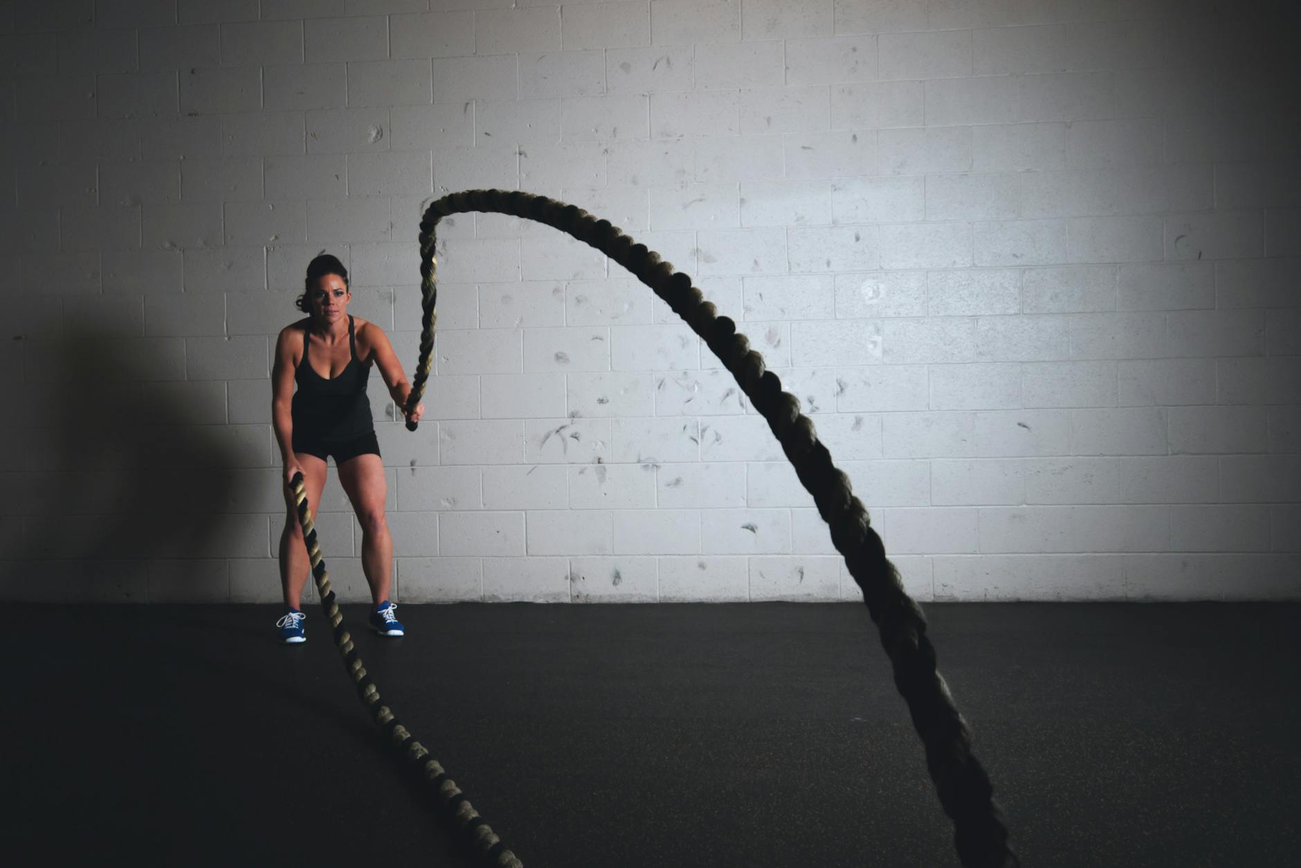 A focused woman performs a dynamic battle rope exercise in a gym setting, demonstrating strength and fitness. - planet fitness workout