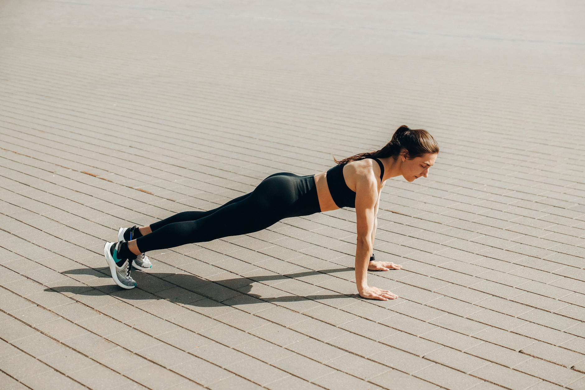 Woman doing push-ups outdoors in activewear, promoting fitness and healthy lifestyle. - planet fitness workout